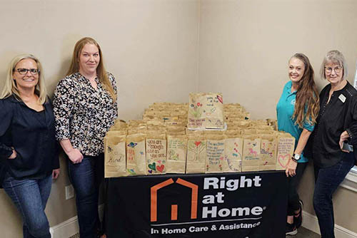 Two women posing on each side of a Right at Home logo table full of Kids Meals donations