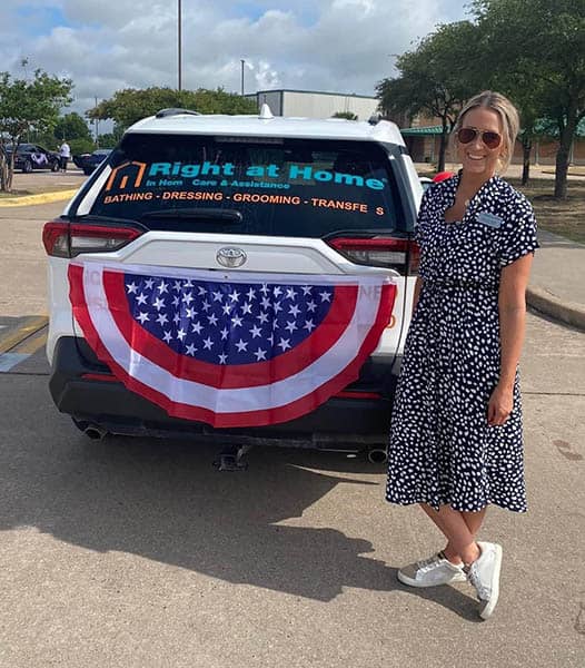 One of the female Right at Home of Brenham, TX staff members standing next to the Right at Home Brenham car, decorated for a parade