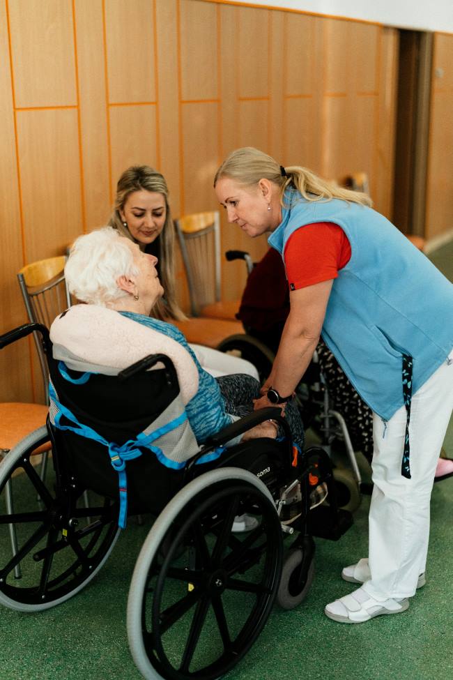 two women helping a woman in a wheelchair 