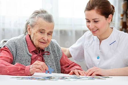 Caregiver assisting elderly woman solve a jigsaw puzzle