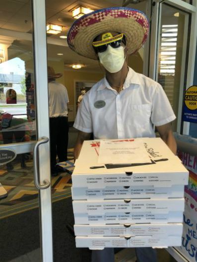 Man wearing a sombrero, while holding a stack of pizza boxes at the Bristal Assisted Living East Meadow, NY
