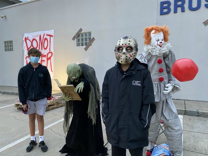 Right at Home volunteering at the Kids Need More Haunted Car Wash at Johnnies Car Wash in Copiague, NY. Two young men volunteering, one wearing a costume, the other in a face mask next to a haunted attractions