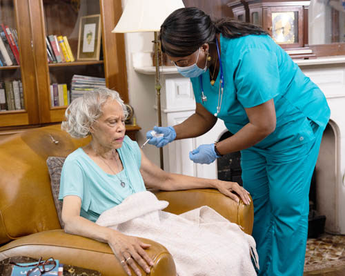 Female Caregiver Giving Skilled Nursing Care To Senior Woman