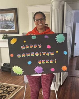 Caregiver Kaleah Scott holding a "Happy Caregiver Week" sign