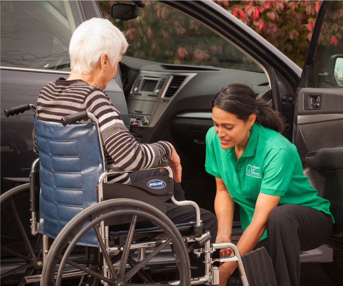 Caregiver helping senior client out of car and into wheelchair