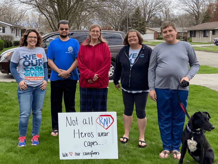 Five people and one dog standing around a yard sign Honoring our Right at Home caregiver heroes