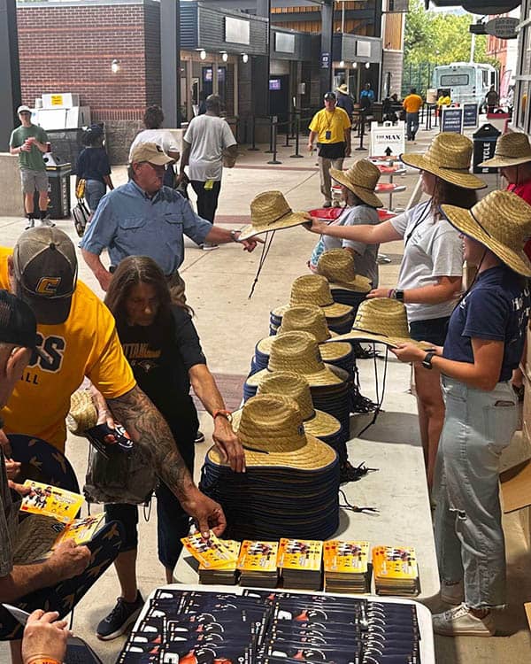 A group of ladies handing out Right at Home hats to football fans.