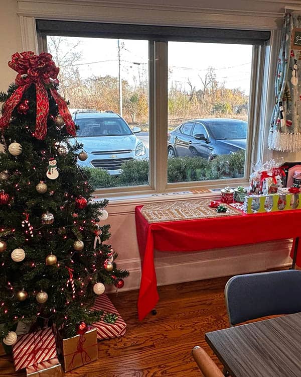 A Christmas tree is standing near a window. A small table holds gifts.