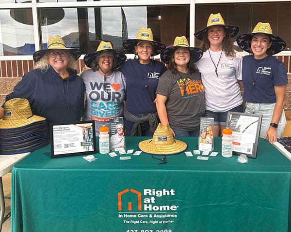 A group of ladies standing behind a table wearing Right at Home hats.