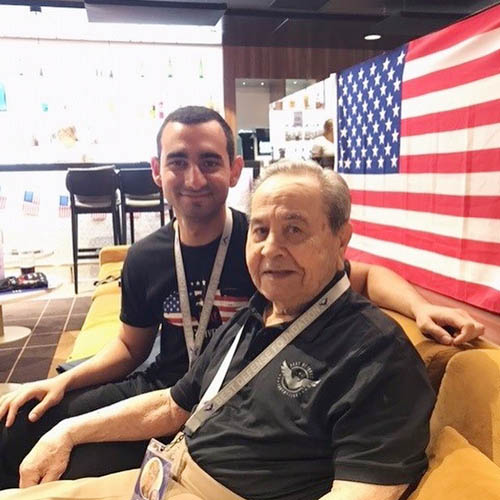 Senior Male Veteran Seated with Young Male Caregivers in Front of the American Flag