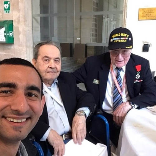 Two Senior Veterans in Wheelchairs with Their Young Male Caregiver's Face Peeking In in the Foreground