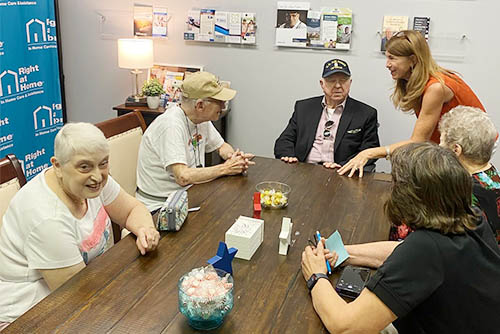 Group photo men and women seniors seated around a table talking while at a Holocaust Survivors and Veterans Gathering