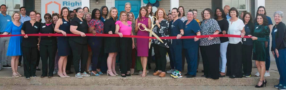 Right at Home Lafayette Open House Row of People Standing as The Ribbon Is Being Cut with Giant Scissors