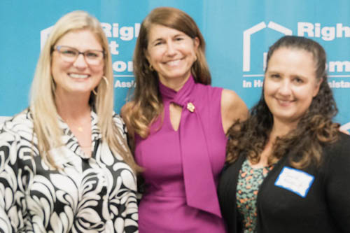 Three Women Pose for a Photo in Front of a Wall of Right at Home Logos at an Open House Event in Lafayette