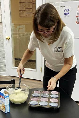 Female Caregiver Scooping Muffin Batter Into A Pan