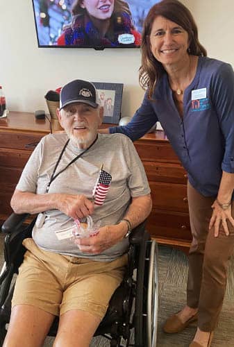 Female Caregiver Posing With a Seated Senior Veteran Holding Gift Cookies