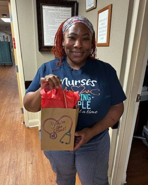 A smiling, African-American, female nurse holding a gift bag.