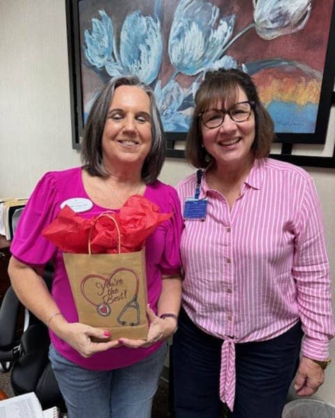 Two smiling female nurses. One is holding a gift bag.