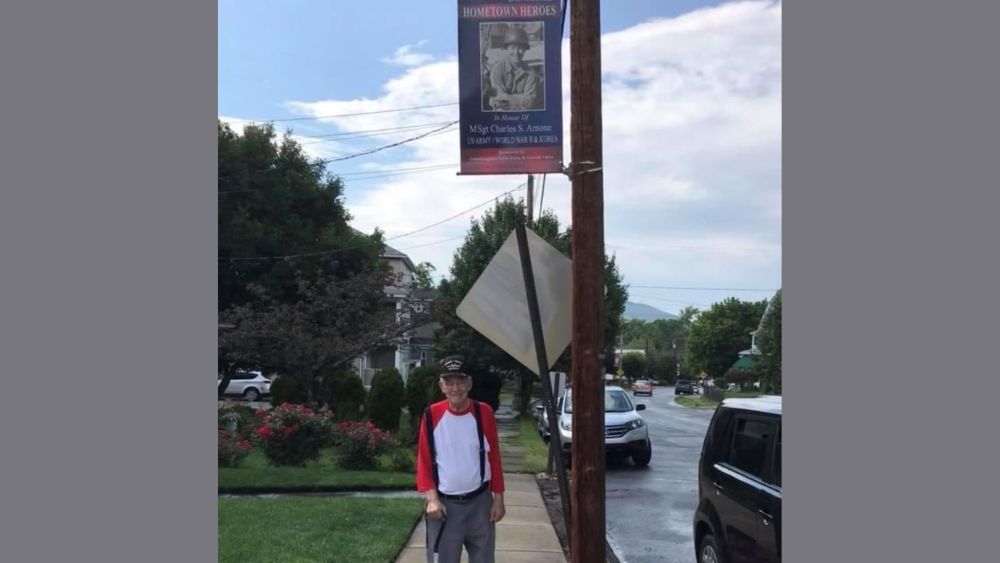 image of charles, veteran standing under flag on pole showing his military service with a gray background