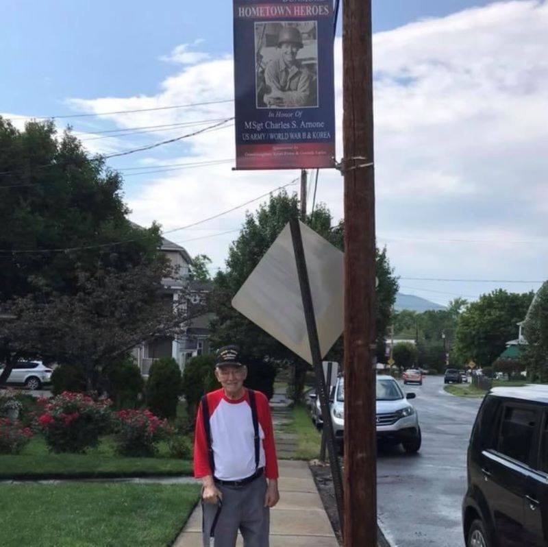 Charles, veteran, standing under flag with his military service years and photo on it