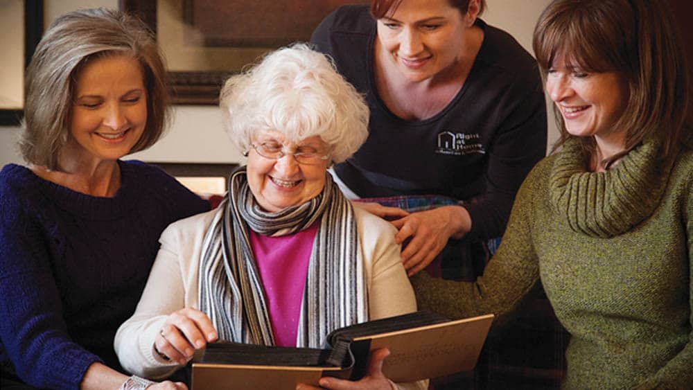 Senior woman with photo album surrounded by family and her female caregiver