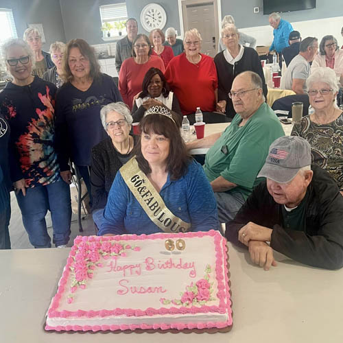 Senior Birthday Girl Sitting with a Crown and Sash on and a Big Sheet Cake in Front of Her