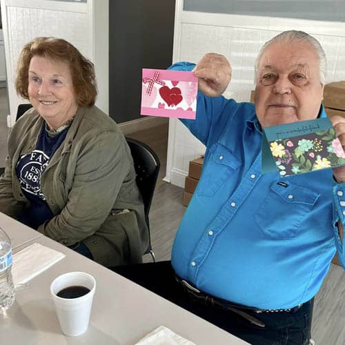 Gentleman Sitting at a Table Holding Up a Couple Greeting Cards He Wrote