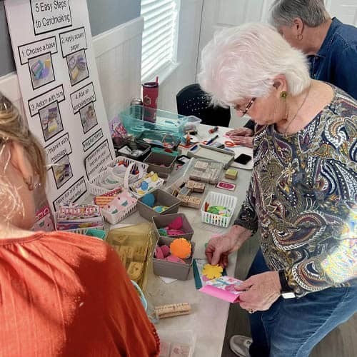 Group of Seniors Around a Craft Supply Table Getting Supplies to Write Greeting Cards