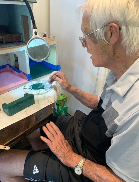 Older gentleman painting dollhouse