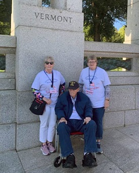 Senior man in wheelchair is accompanied by two females. They are next to a statue that says "Vermont".