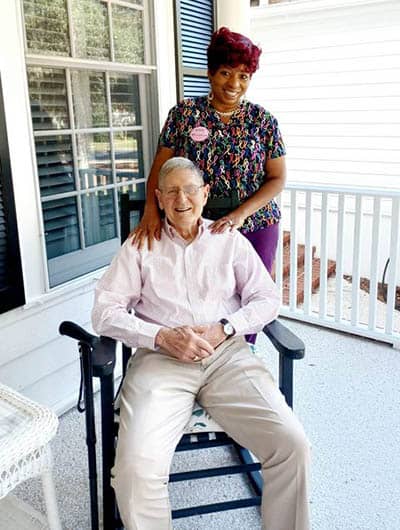 Right at Home caregiver Jenny standing behind a seated client outside on a porch 