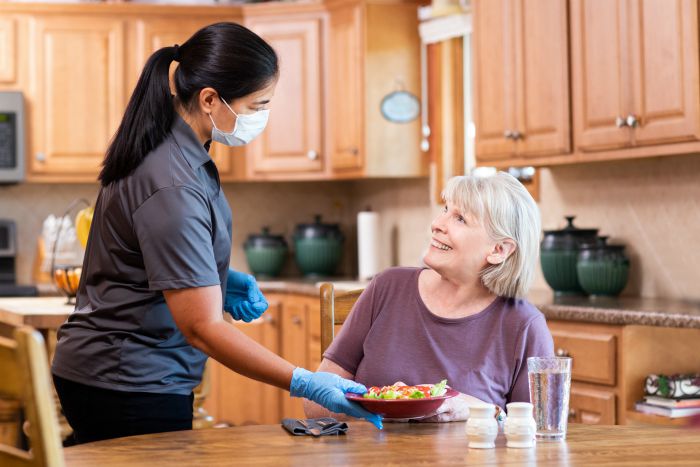 female caregiver serving a salad to a senior woman in the kitchen