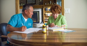 Male caregiver helping a senior female count out medications for the week while sitting at a table