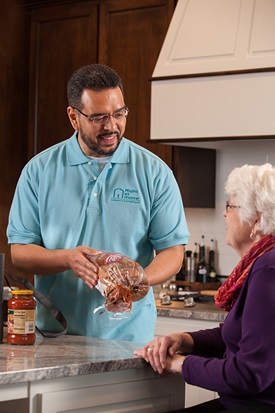 Male Right at Home caregiver preparing a meal for a senior female in a kitchen