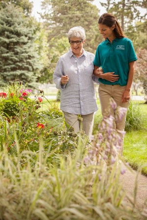 Female caregiver escorting a female senior on a path next to flowers, outside