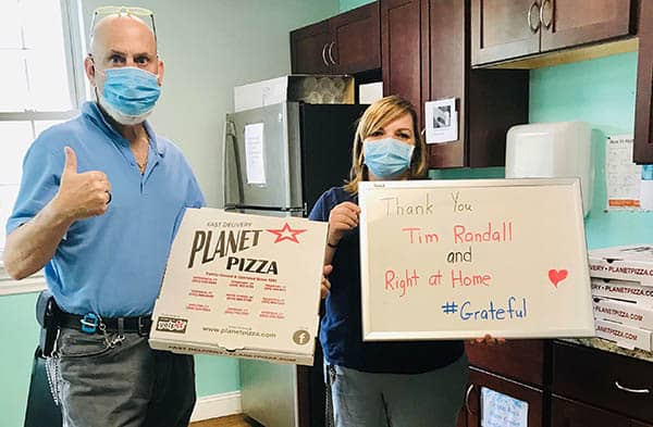 Benchmark Lighthouse Pizza Drop with Kathleen Bizer and another male employee holding pizza and a sign thanking Right at Home for the food.