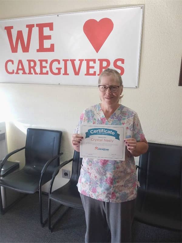 Crystal standing in front of the We Love Our Caregivers sign with her certificate for Employee of the Month 