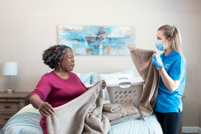 female caregiver folding laundry with a senior female in a bedroom