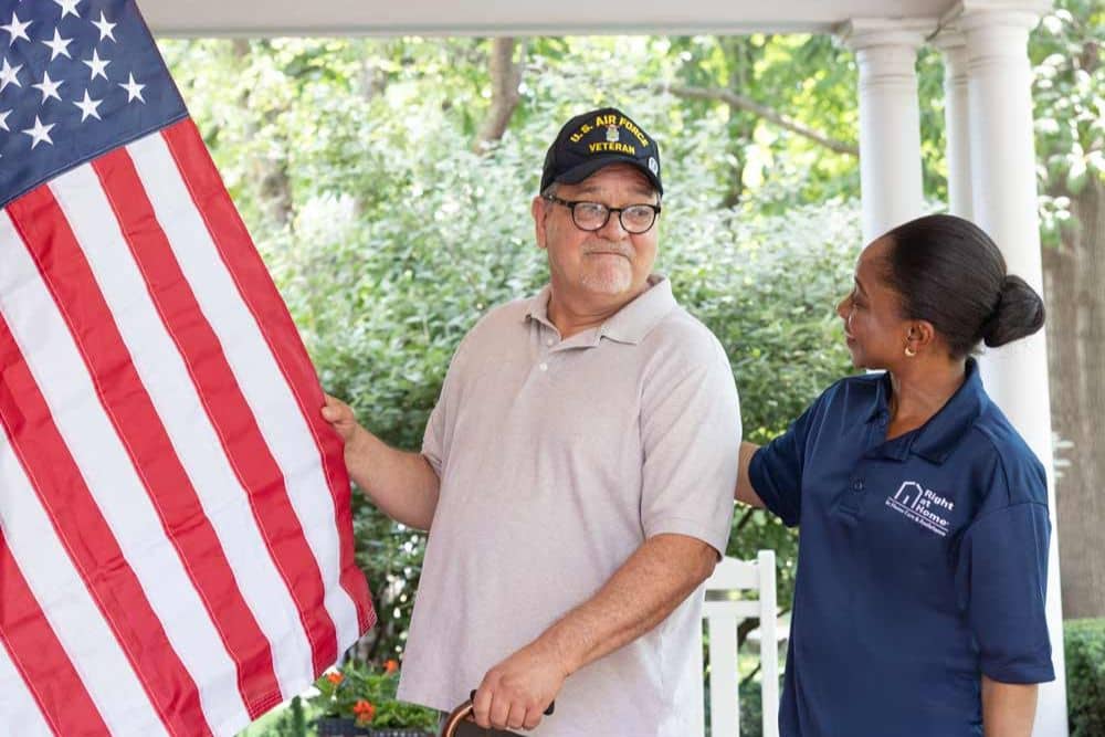 Senior veteran male client holding onto American flag with black female caregiver standing beside him