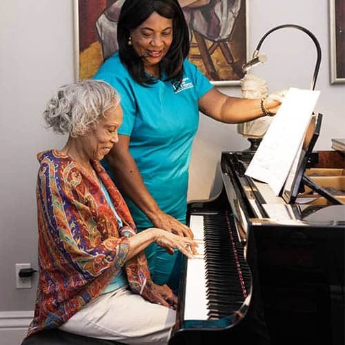 African American Senior Woman Playing Piano with Female Caregiver