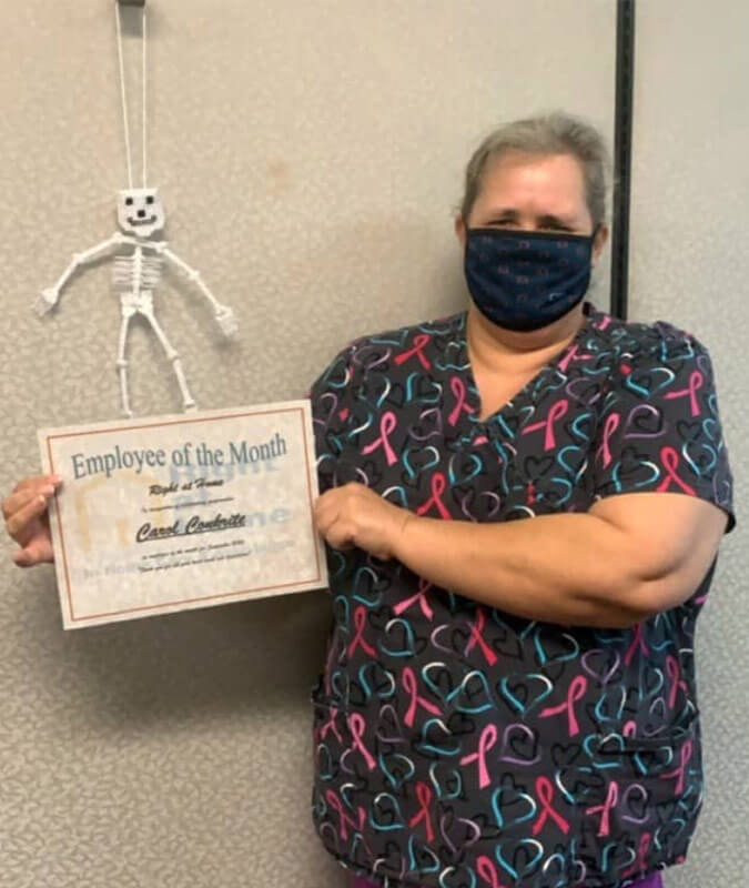 Photo of Carol, caregiver, with face mask on, holding Employee of the Month certificate