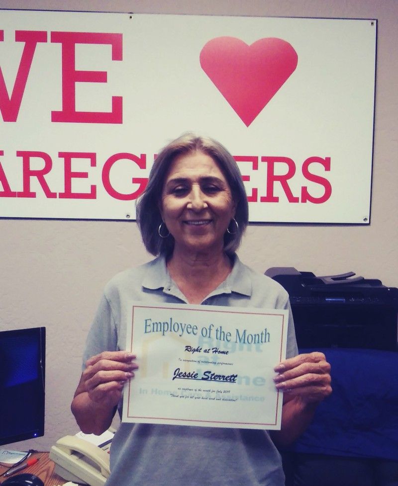 Jessie S. holding Employee of the Month certificate and standing in front of sign that says, 'We Love Our Caregivers'