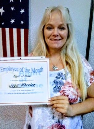 Joyce holding Caregiver of the Month certificate in front of American Flag hanging vertical on wall in background