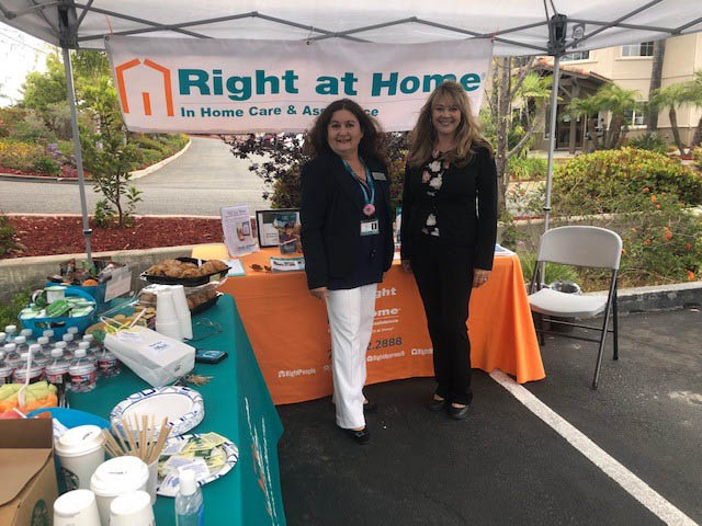 Carmen and Theresa standing in front of a table and Right at Home banner under a tent