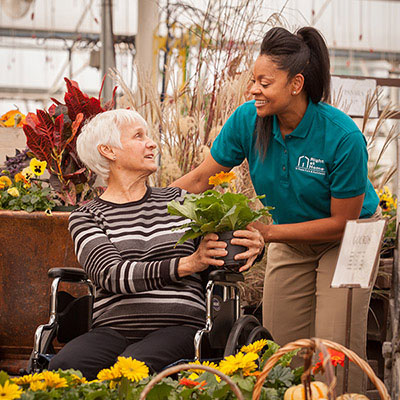 Female Caregiver Shopping With Female Client In Wheelchair At Garden Center
