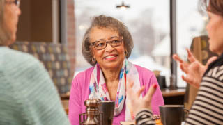A client listening intently to her caregiver as they talk over coffee.