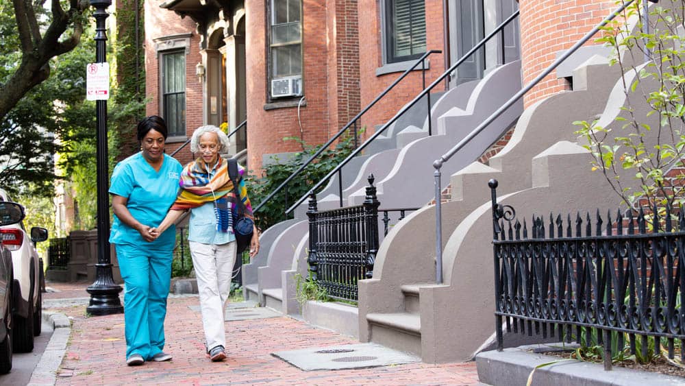 female right at home caregiver walking hand in hand with female senior client down the sidewalk