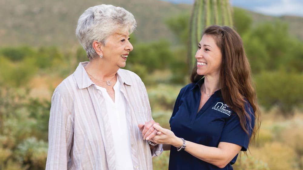 Female Right at Home caregiver standing hand in hand with senior female client outside