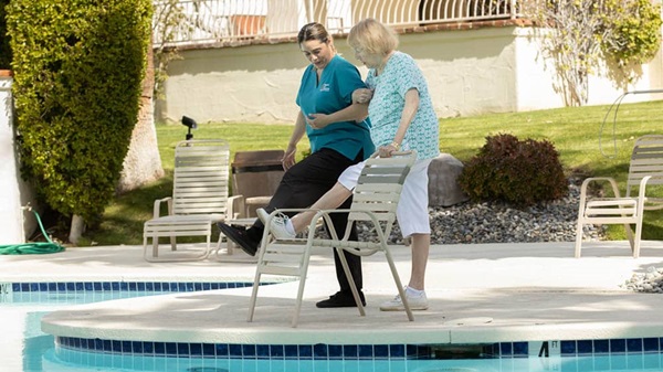 A female Right at Home caregiver is helping a senior female exercise next to a pool outside