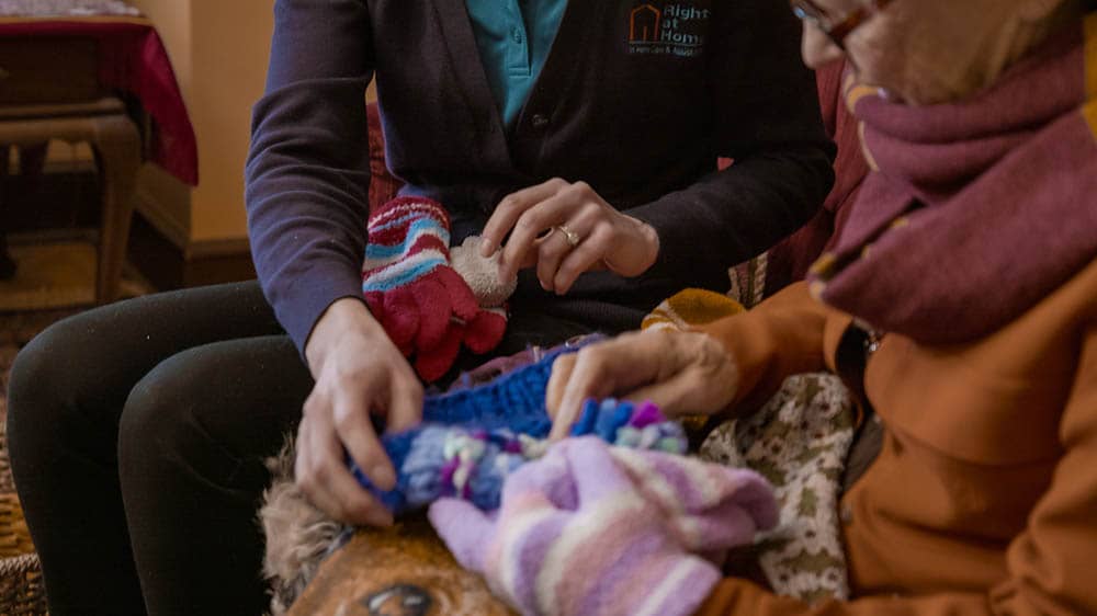 a female Right at Home caregiver helping a senior female client try on winter gloves as they prepare a winter safety kit